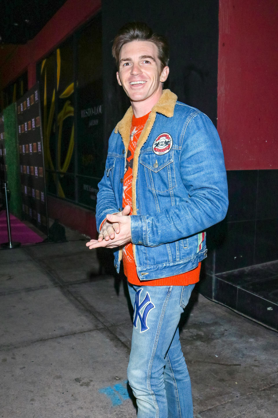 Drake Bell wearing a red t-shirt, jeans, and a jean jacket