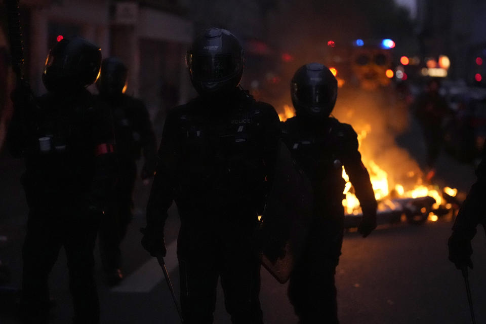 Members of the BRAV-M police brigade march in a street where garbage cans burn after French President Emmanuel Macron tried to diffuse tensions in a televised address to the nation, Monday, April 17, 2023 in Paris. Emmanuel Macron said Monday that he heard people's anger over raising the retirement age from 62 to 64, but insisted that it was needed. (AP Photo/Thibault Camus)