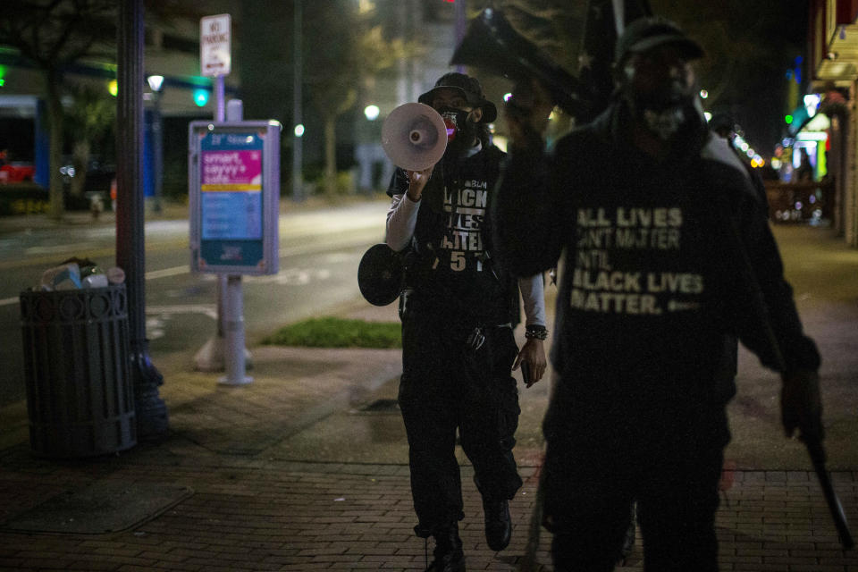 Aubrey "Japharii" Jones, left, walks on the sidewalk on Atlantic Ave. Saturday March 27, 2021 in Virginia Beach, Va.. Overnight shootings near the Atlantic oceanfront in Virginia Beach left two people dead and eight wounded in a scene described by authorities on Saturday as “very chaotic.” (AP Photo/John C. Clark)