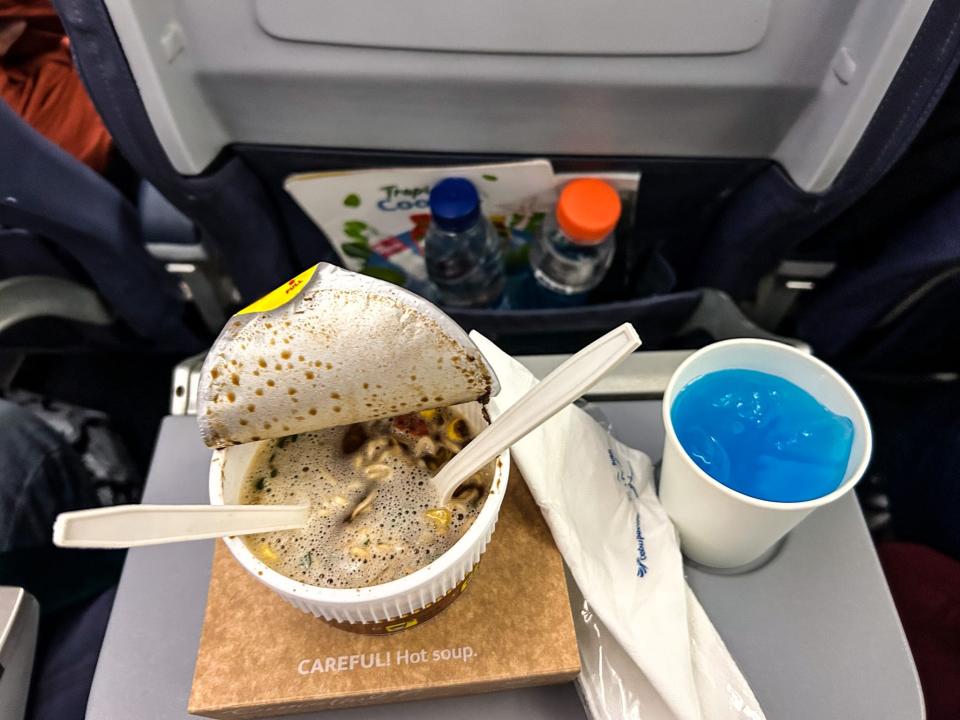 A cup of instant noodles and a cup of blue gatorade on a fold-down tray.