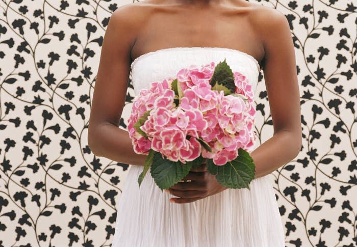 Woman smiles warmly, holding pink hydrangeas in front of a floral-patterned background