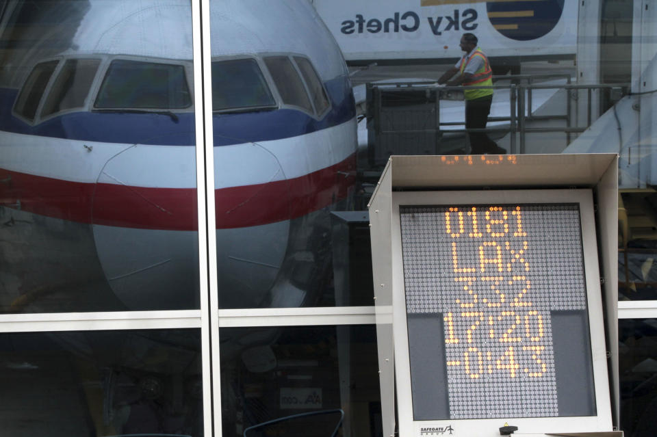 In this Wednesday, Aug. 1 2012 photo, a countdown to departure clock is framed by a reflection of an American Airlines fleet clerk servicing an airplane at JFK International airport in New York. Travelers still have to put up with packed planes, rising fees and unpredictable security lines, but they are missing fewer business meetings or chances to tuck their kids into bed. Nearly 84 percent of domestic flights arrived within 15 minutes of their schedule time in the first half of the year, the best performance since the government started tracking such data in 1988. (AP Photo/Mary Altaffer)