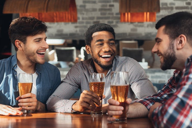 Three men smiling and chatting around a table at a pub