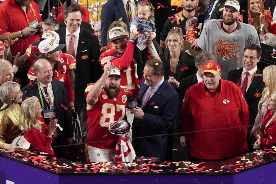 Travis Kelce smiles and yells while holding the Vince Lombardi Trophy and is interviewed by Jim Nantz.