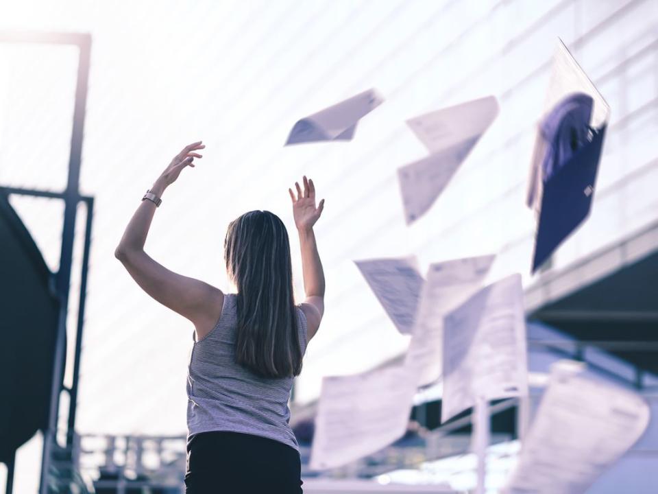 Business woman throwing work papers in the air. Stress from workload. Person going home or leaving for vacation. Employee got fired. Job or project done. Difficult workday over.