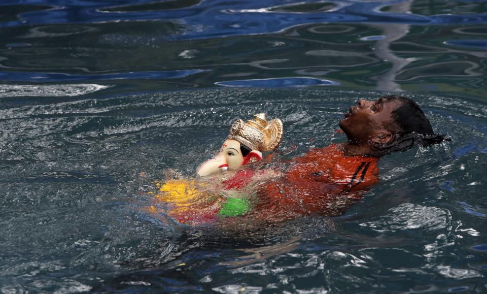 A volunteer immerses in an artificial pond an idol of elephant headed Hindu god Ganesh that was worshipped during the Ganesh Chaturti festival in Mumbai, India, Sunday, Aug.23, 2020. India’s coronavirus caseload topped 3 million on Sunday, with the country leading the world in new infections as the disease marched through impoverished rural areas in the north and the wealthier but older populations of the south. (AP Photo/Rajanish Kakade)