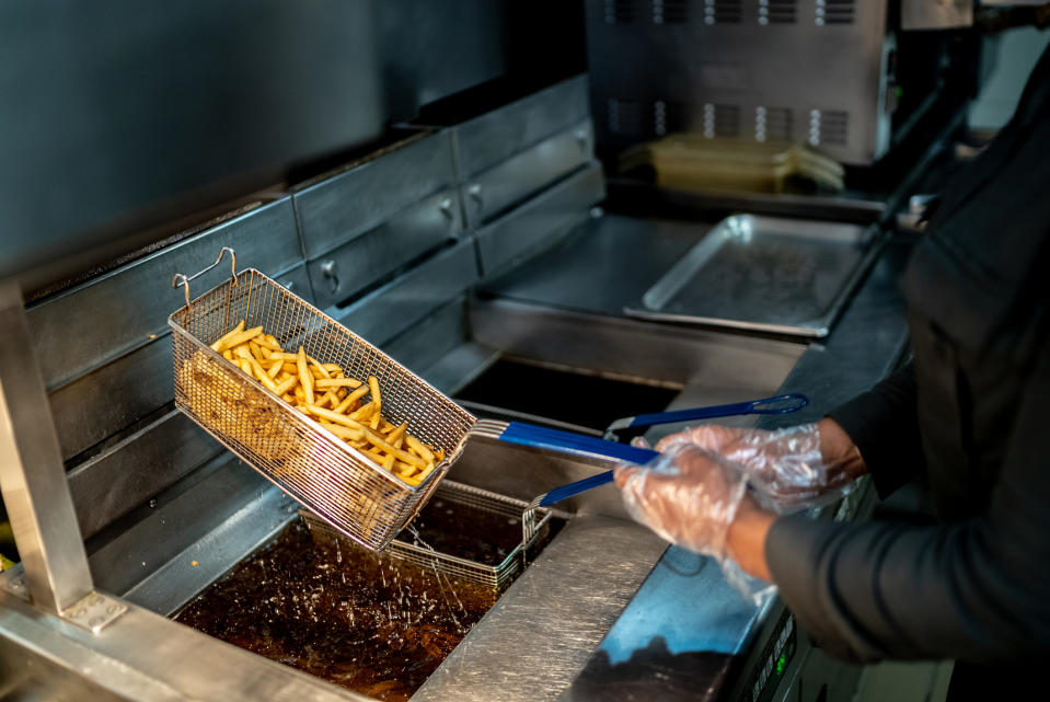 A food service worker is taking fries out of the fryer