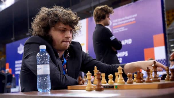 PHOTO: Hans Niemann plays a match at the World Rapid and Blitz Championships as Magnus Carlsen watches other matches from behind. (ABC News)