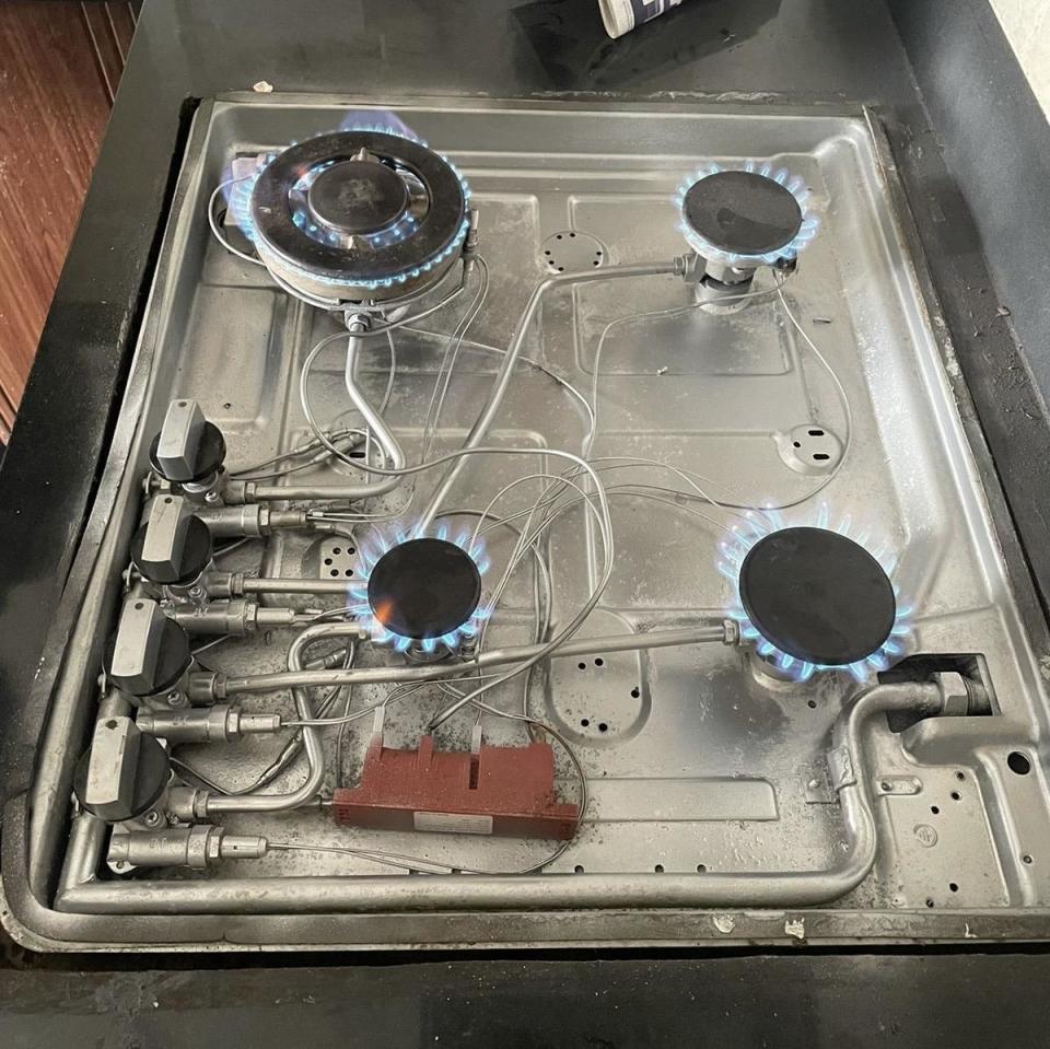 A stovetop with four burners lit, showing exposed wiring and connections