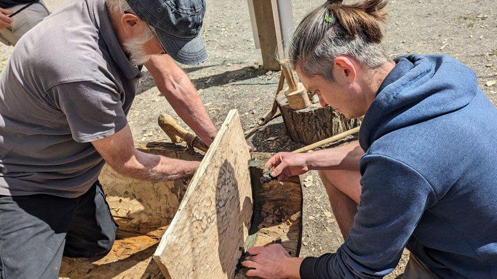 A male volunteer on the left and James Dilley on the right fitting a transom board to the end of one of the log boats