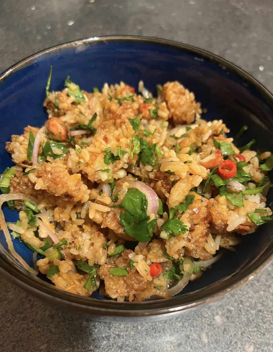 A bowl of fried rice with vegetables and garnished with herbs