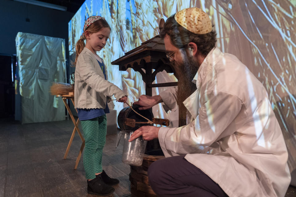 Wearing a kippah with a matzah design, Rabbi Levi Raskin, right, shows a first grade student from Milton Gottesman Jewish Day School of the Nation's Capital, how water could be drawn from a well as part of a "Model Matzah Factory" field trip at the JCrafts Center for Jewish Life and Tradition in Rockville, Md., Thursday, April 18, 2024, ahead of the Passover holiday which begins next Monday evening. (AP Photo/Jacquelyn Martin)