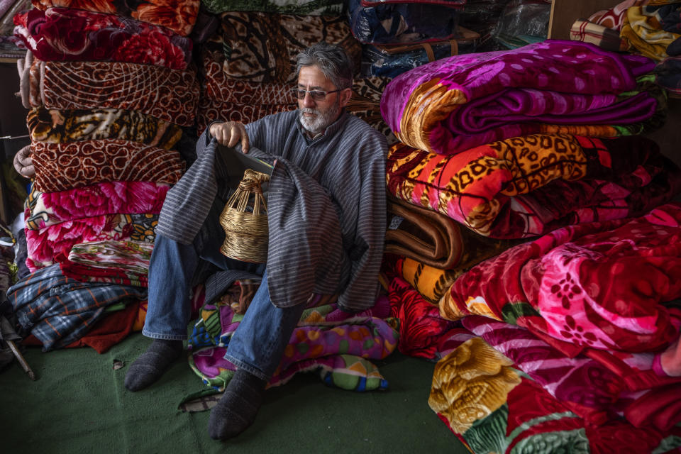 Mohammad Shafa, a Kashmiri shopkeeper selling blankets, displays the handling of a kanger in Srinagar, Indian controlled Kashmir, Friday, Jan. 5, 2024. For locals, the major source of heat is the kanger, a pot filled with hot coal embers that is tucked inside their pheran, a traditional knee-length cloak. Almost ensnared by its warmth, people only step outside for work and other essentials. (AP Photo/Dar Yasin)