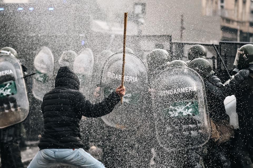 Un hombre esgrime un palo frente a un grupo policías antidisturbios.