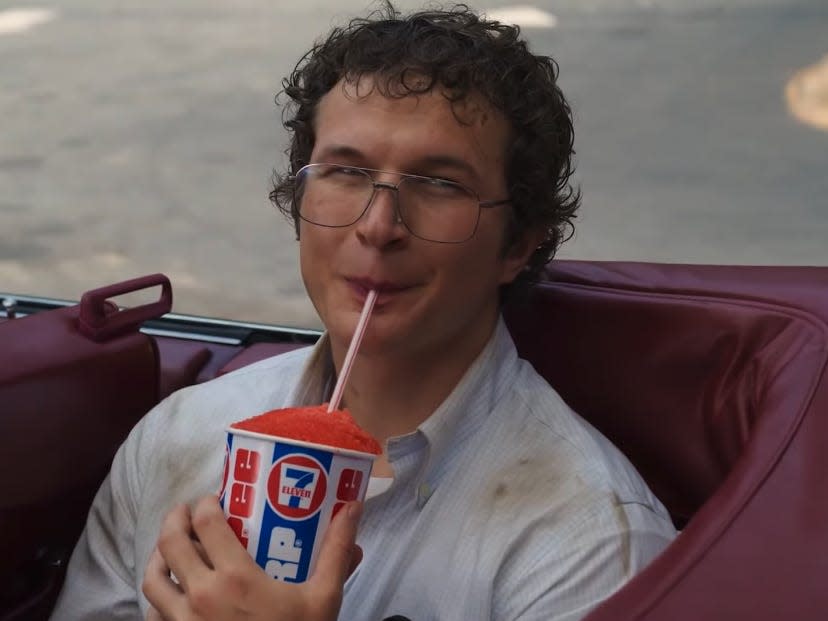 alexei in stranger things sipping on a slurpee in the back of a car, looking smug