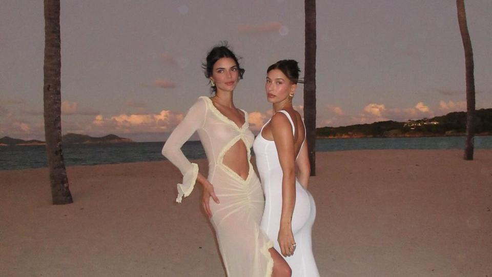 Hailey Bieber and Kendall Jenner pose on a sandy beach in matching cream and white gowns