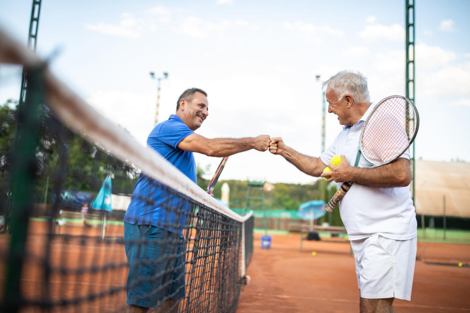 Two senior men greeting each other with fist bump on tennis court