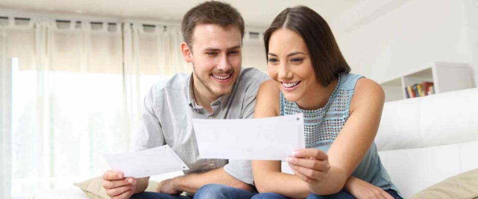 Happy young couple looking and checking bills on a couch at home