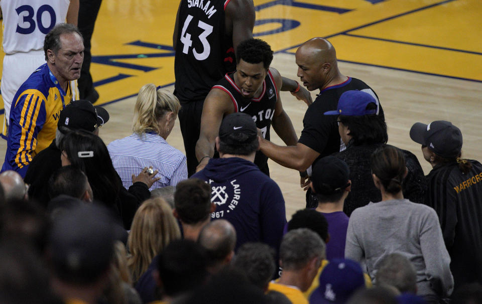 Toronto Raptors guard Kyle Lowry, middle, gestures next to referee Marc Davis (8) near the front row of fans during the second half of Game 3 of basketball's NBA Finals between the Golden State Warriors and the Raptors in Oakland, Calif., Wednesday, June 5, 2019. A fan seated courtside for Game 3 of the NBA Finals was ejected after shoving Lowry when the Raptors star crashed into a row of seats while trying to save a ball from going out of bounds on Wednesday night. (AP Photo/Tony Avelar)