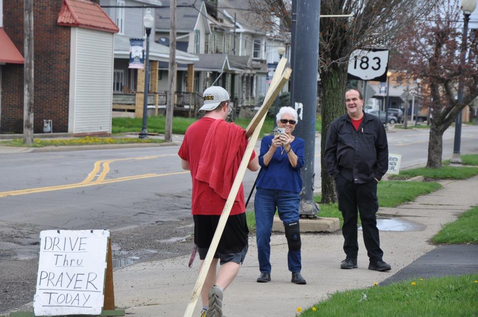 Mason Polinori, 27, of Alliance, finishes a 2.5-mile walk while carrying a cross on Thursday, April 11, 2024, at the Alliance First Assembly of God Church. Shirley Rosser, 77, and Shawn Bodendorfer, 53, members of the church, greet him.