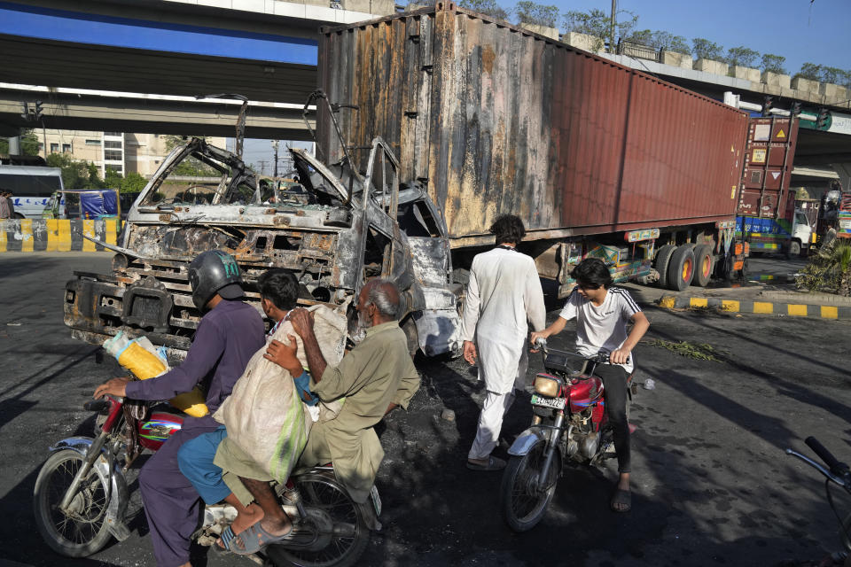 Varias personas en motocicleta pasan por delante de un camión calcinado durante enfrentamientos entre la policía y partidarios del ex primer ministro Imran Khan, en Lahore, Pakistán, el 11 de mayo de 2023. (AP Foto/K.M. Chaudary)