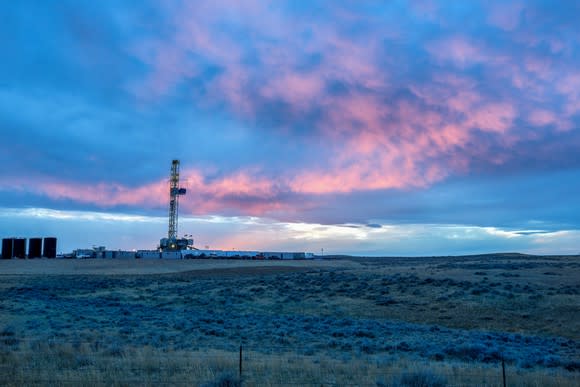 A drilling rig in a prairie field at dusk.