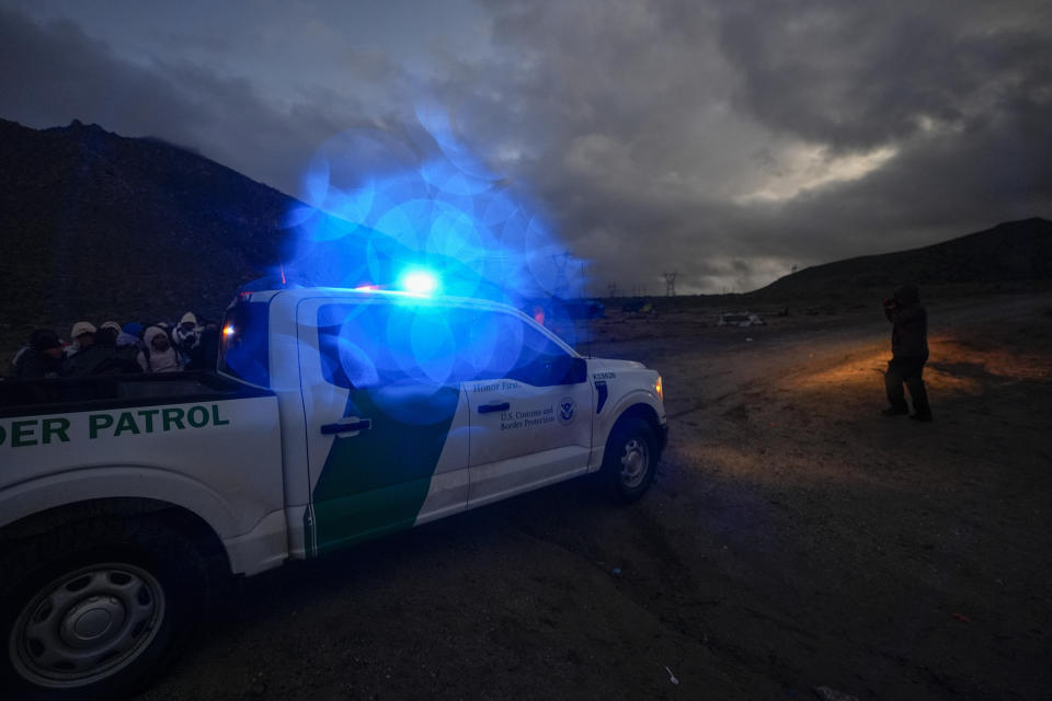 A Border Patrol vehicle parks in front of a group of asylum-seeking migrants as they line up in a makeshift, mountainous campsite to be processed after crossing the border with Mexico, Friday, Feb. 2, 2024, near Jacumba Hot Springs, Calif. (AP Photo/Gregory Bull)