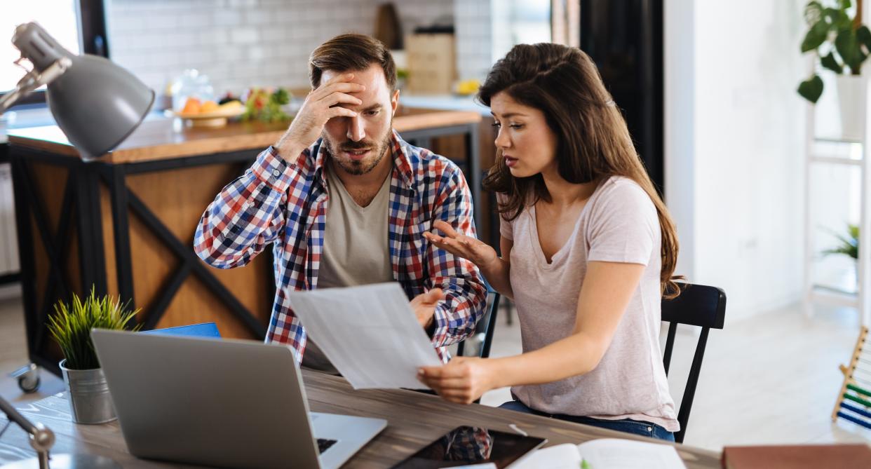 Couple sit at table and argue over money. (Getty Images)