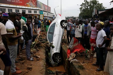 People look at a car in a sewer after a flood in Abidjan, Ivory Coast, June 19, 2018. REUTERS/Luc Gnago