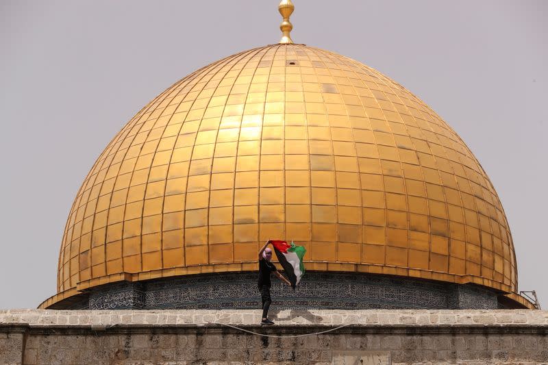 A Palestinian man holds a flag as he stands at the compound that houses Al-Aqsa Mosque in Jerusalem's Old City