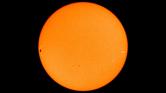 The planet Mercury transiting in front of the sun, as captured by a NASA satellite. Mercury is near the center of the image, while dark sunspots appear near the edges.