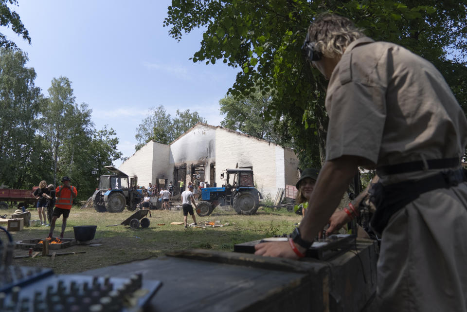 A DJ at work while young volunteers clear debris from a building destroyed by a Russian rocket in the village of Yahidne, Chernihiv Region, Ukraine, Sunday, July 24, 2022. In a village in northern Ukraine, devastated by Russian occupation only months ago, a techno party in a bombed-out building has brought together more than 200 young people who have found a novel way to help rebuild their country. (AP Photo/Roman Hrytsyna)