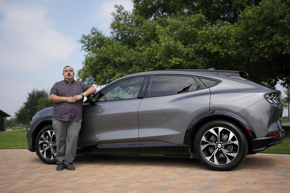 Jose Valdez, 45, who owns three EVs, poses with his Mustang Mach-E, Thursday, May 9, 2024, in San Antonio. Many Americans still aren’t sold on going electric for their next car purchase. High prices and a lack of easy-to-find charging stations are major sticking points, a new poll shows. Valdez owns three EVs, including a new Mustang Mach-E. With a tax credit and other incentives, the sleek new car cost about $49,000, Valdez said. He thinks it's well worth the money. (AP Photo/Eric Gay)