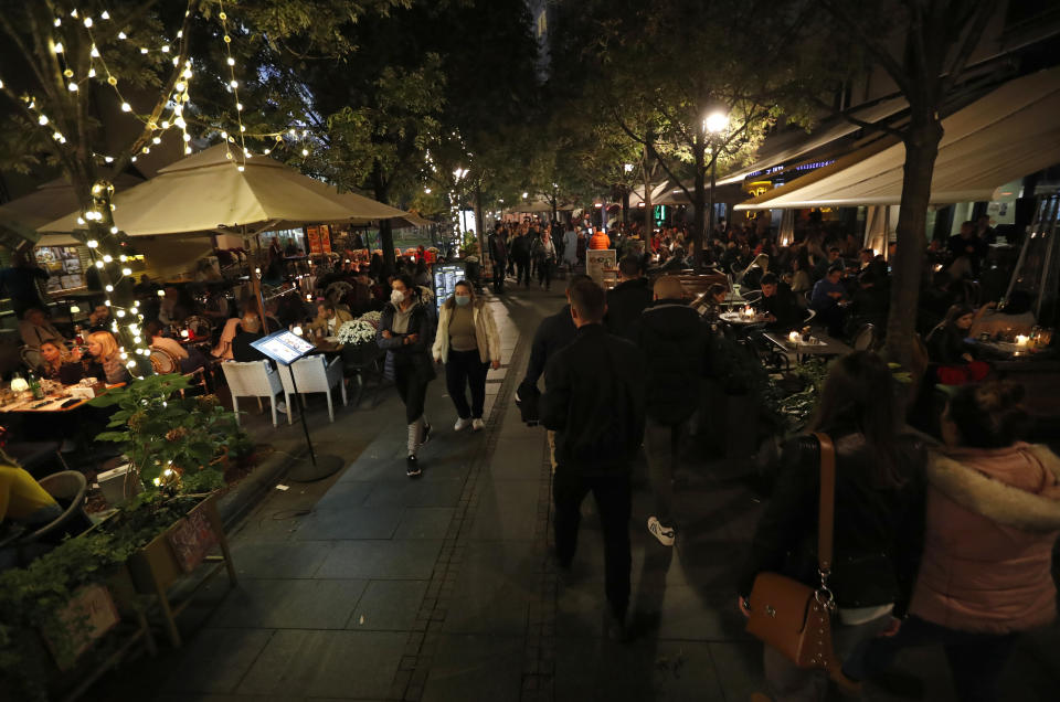 People walk along the street crowded with coffee shops and clubs full of guests in downtown Belgrade, Serbia, Friday, Oct. 23, 2020. In much of Europe, city squares and streets, be they wide, elegant boulevards like in Paris or cobblestoned alleys in Rome, serve as animated evening extensions of drawing rooms and living rooms. As Coronavirus restrictions once again put limitations on how we live and socialize, AP photographers across Europe delivered a snapshot of how Friday evening, the gateway to the weekend, looks and feels. (AP Photo/Darko Vojinovic)