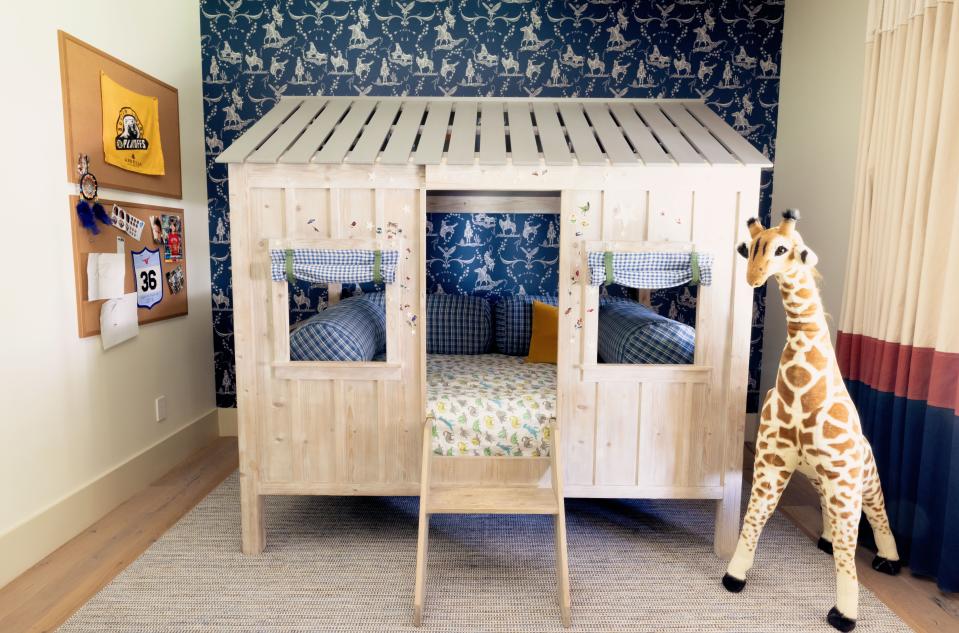 Shepherd sleeps in an RH Kids Cabin Bed set against blue cowboy-print wallpaper from Walnut. His curtains were custom made of dyed canvas by Older Brother.