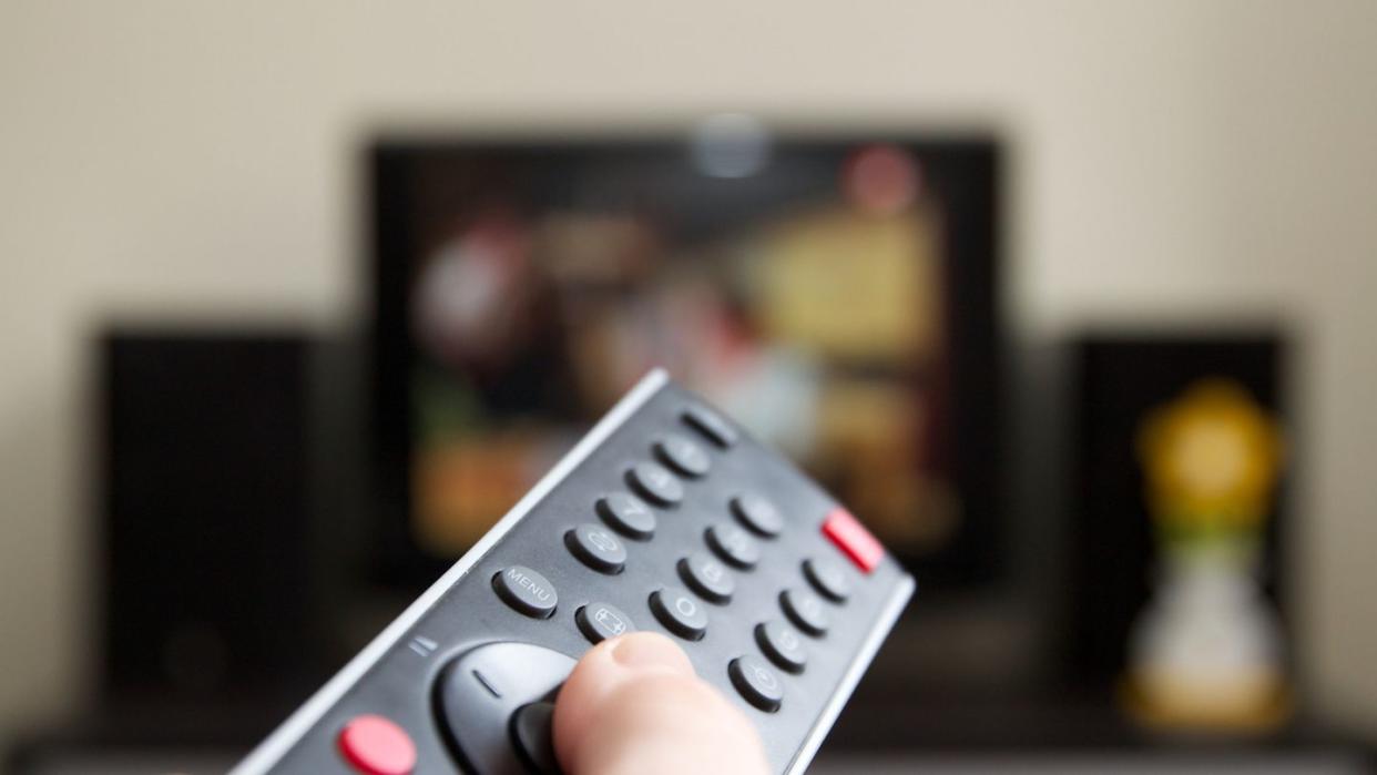 human hand holding remote control changing channels with television set