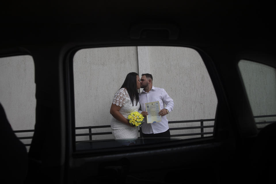 Ayrton (derecha) y Natasha se besan tras casarse en el drive-thru de una oficina de registro, en el vecindario de Santa Cruz, en Río de Janeiro, Brasil, el 28 de mayo de 2020. Las parejas que no pueden tener un enlace tradicional por la pandemia, recurren a este tipo de bodas rápidas. (AP Foto/Silvia Izquierdo)