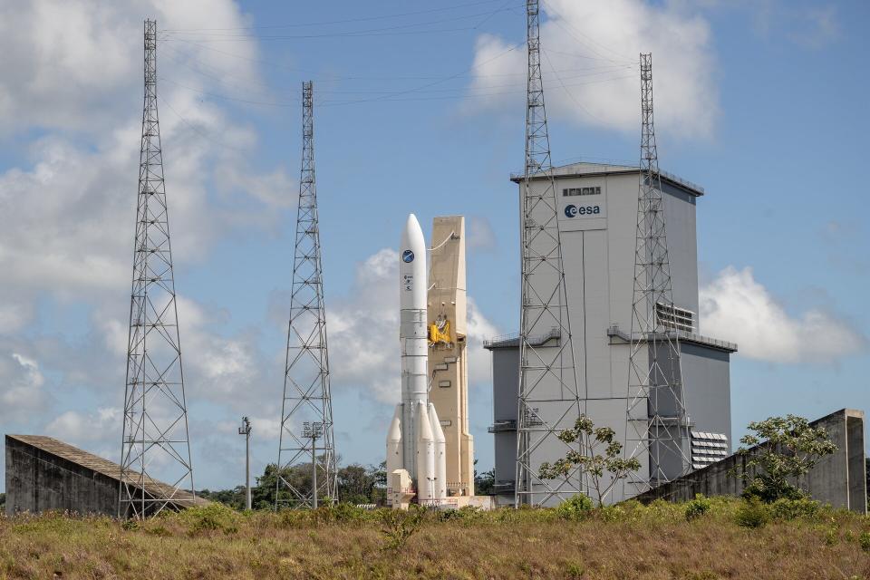 Europe's new Ariane 6 stands at the launchpad in front of a blue sky and a grassy foreground.