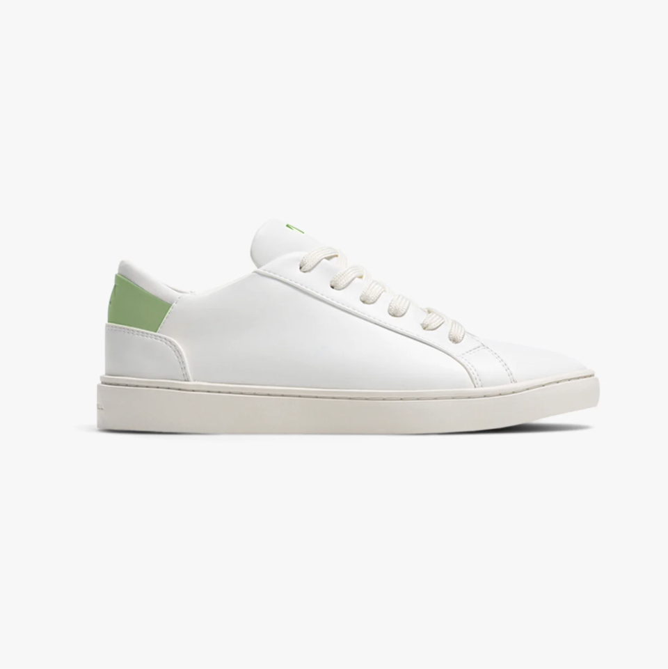 A white sneaker with green detailing in the back