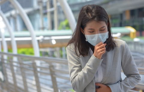 Sick woman wearing a face mask - Credit: Getty