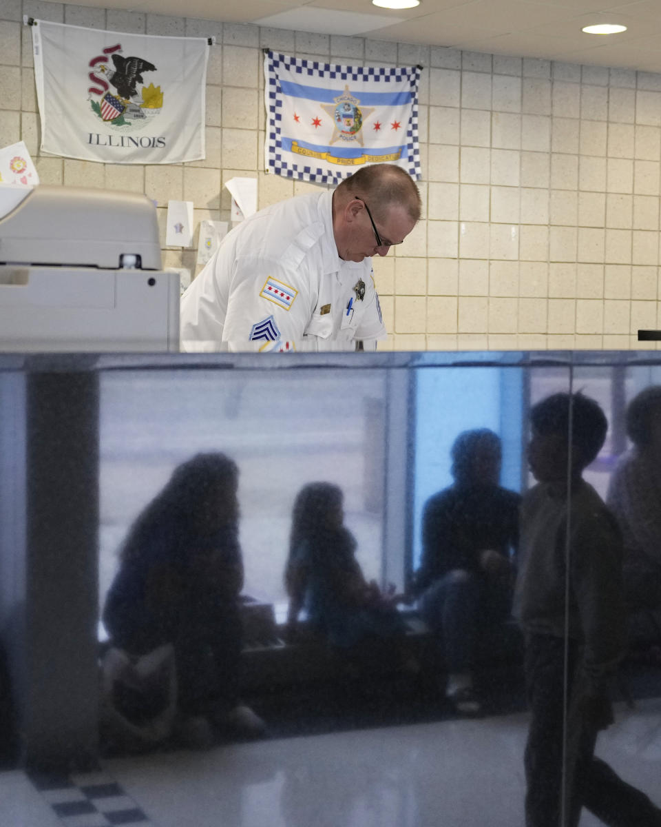 Chicago Police Department Desk Sargent Greg Noncz works as migrants from Venezuela are reflected in a marble wall while taking shelter in the department's 16th District station on Monday, May 1, 2023. Chicago has seen the number of new arrivals grow tenfold in recent days. Shelter space is scarce and migrants awaiting a bed are sleeping on floors in police stations and airports. (AP Photo/Charles Rex Arbogast)