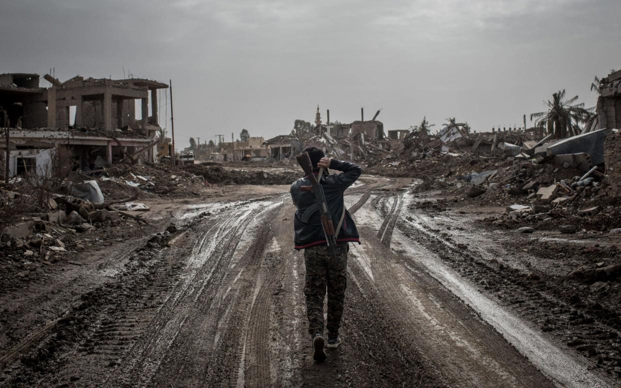 A Syrian Democratic Forces (SDF) fighter walks through the destruction of a town liberated from Isil - Getty Images Europe