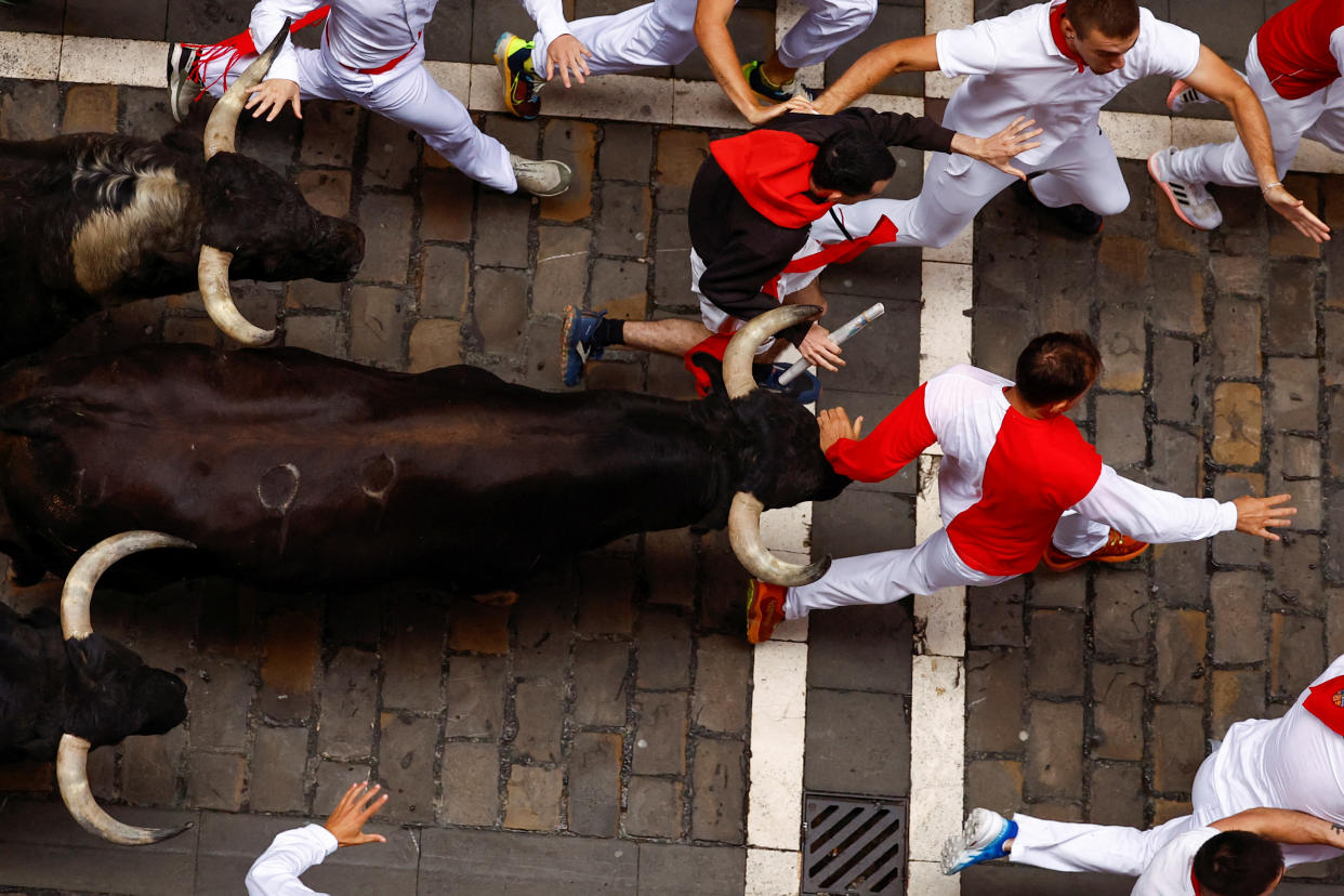 Running bulls can be seen closing in on revelers who are trying to run ahead of the animals.