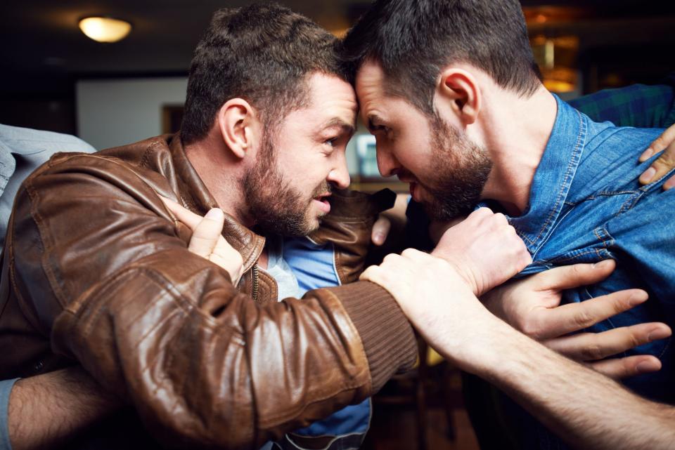 Waist up shot of two aggressive drunken men looking at each other furiously and quarrelling while their friends trying to stop fight in pub.