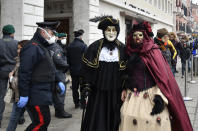 A policeman wearing a sanitary masks passes by two revelers in Venice, Sunday, Feb. 23, 2020. Italian authorities have announced they are shutting down Venice's famed carnival events in a bid to stop the spread of the novel virus, as numbers of infected persons in the country have soared to at least 133, the largest amount of cases outside Asia. (AP Photo/Luigi Costantini)