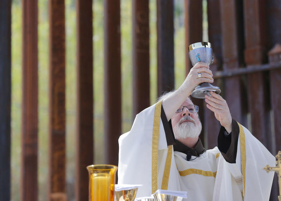 Cardinal Sean O'Malley prepares to serve communion as he leads mass, Tuesday, April 1, 2014, along the international border wall in Nogales, Ariz. O'Malley and several Bishops who serve along the U.S./Mexico border were visiting the border town to bring awareness to immigration reform and to remember those who have died trying to cross the border in years past. (AP Photo/Matt York)