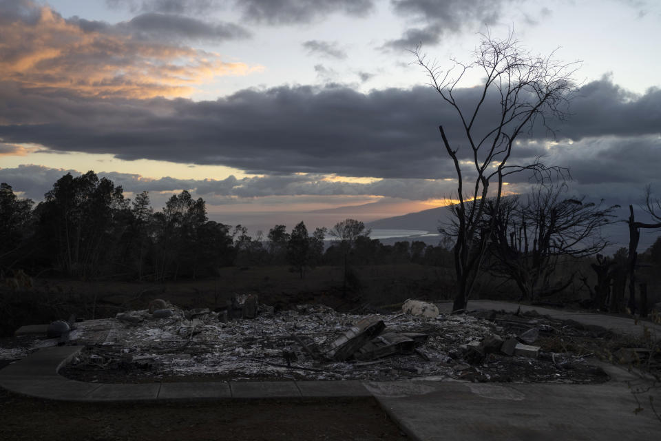 A home burned to ashes is seen in foreground as the sunset colors the sky in Kula, Hawaii, Tuesday, Aug. 15, 2023, following wildfires that devastated parts of the Hawaiian island of Maui. (AP Photo/Jae C. Hong)
