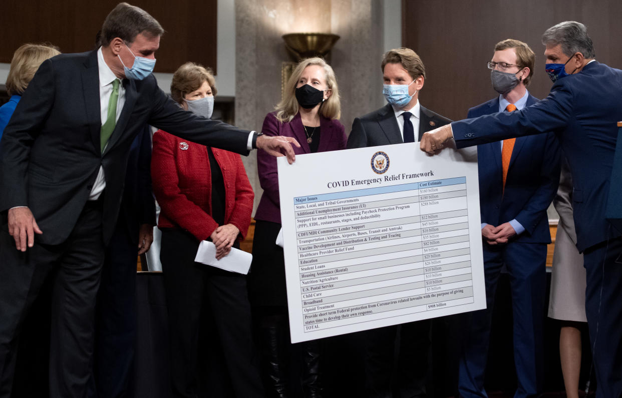 US Senator Joe Manchin (R), Democrat of West Virginia, hands a poster describing a proposal for a Covid relief bill to US Senator Mark Warner (L), Democrat of Virginia, alongside a bipartisan group of Democrat and Republican members of Congress as they announce the proposal on Capitol Hill in Washington, DC, on December 1, 2020. (Photo by SAUL LOEB / AFP) (Photo by SAUL LOEB/AFP via Getty Images)