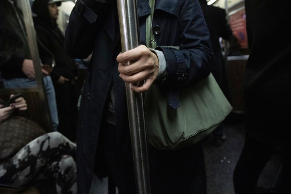 A commuter holds on to a vertical pole as she rides the subway, Wednesday, March 4, 2020, in New York.