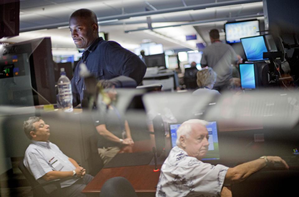 In this Friday, Sept. 20, 2013 photo, a Delta Air Lines employee, top left, works in the Operations Customer Center as airport chaplain Deacon James O'Malley, right, of Chicago, is reflected in a window while attending the International Association of Civil Aviation Chaplains' annual conference at the airline's headquarters, in Atlanta. Airports are mini-cities with their own movie theaters, fire departments and shopping malls. Many also have chapels, which are staffed by a mix of 350 part- and full-time chaplains worldwide who are Catholic, Protestant and, to a lesser extent, Jewish, Muslim or Sikh. (AP Photo/David Goldman)